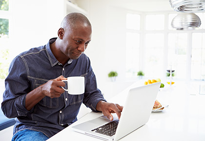 Man sitting drinking coffee while looking at laptop